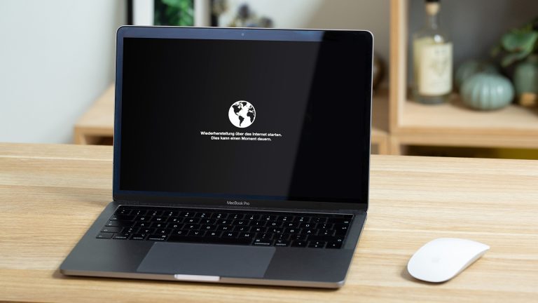 MacBook zurücksetzen Ein aufgeklapptes MacBook steht auf einem Tisch. Auf dem Display ist ein Hinweis zur Wiederherstellung des Systems zu lesen.