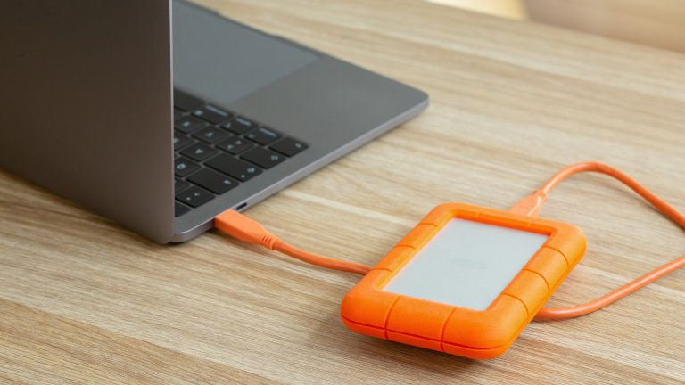 MacBook zurücksetzen Ein aufgeklapptes Macbook steht auf einem Schreibtisch. Daneben liegt eine angeschlossene, externe Festplatte.