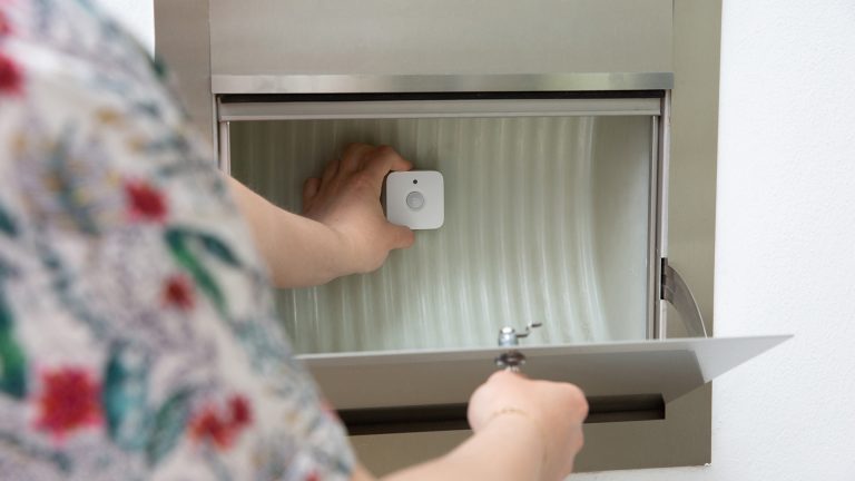 Smarthome-Briefkasten Eine Person befestigt einen Philips Hue Bewegungsmelder in einem Hausbriefkasten.