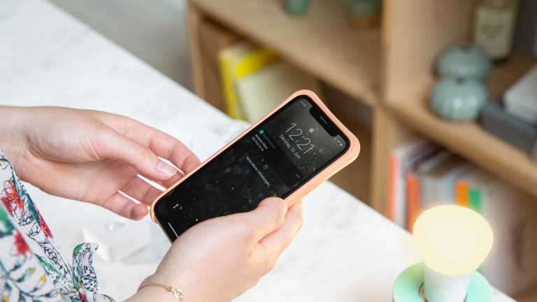 Smarthome-Briefkasten Eine Person steht vor einer gelb aufleuchtenden Philips Hue Lampe. Sie hält ein Smartphone in der Hand, auf dem die Push-Mitteilung “Die Post ist da” zu sehen ist.