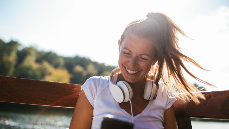 Smartphone im Sommer Eine Frau sitzt an einem See in der Sonne. Sie hält ein Smartphone in der Hand.