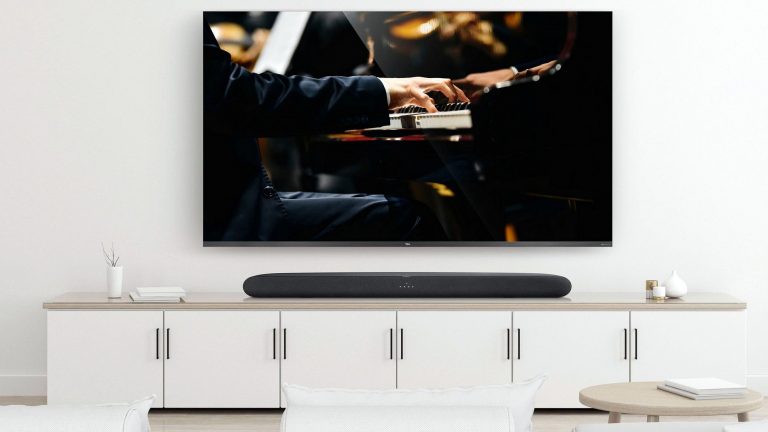 TCL TS6100 An der Wand über einem TV-Sideboard hängt ein TV-Gerät, auf dem Board steht eine Soundbar.