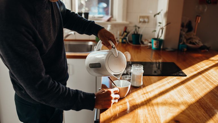 Eine Person gießt heißes Wasser aus einem Wasserkocher in eine Tasse.