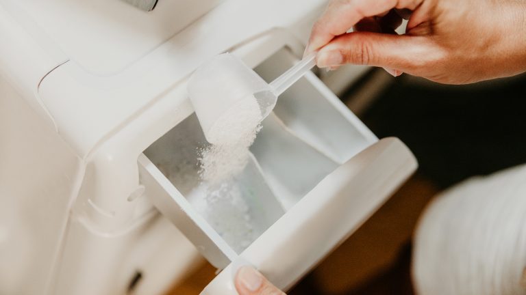 Wasserhärte Eine Person füllt Waschpulver mit einem Löffel in die Waschmaschine ein.