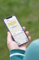 Eine Person hält ein iPhone 12 in der Hand. Darauf ist der Beginn eines Chats bei WhatsApp zu erkennen.