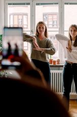 Zwei junge Frauen tanzen eine Choreografie für ein Video. Im Vordergrund ist unscharf ein Smartphone zu erkennen, das die beiden filmt.
