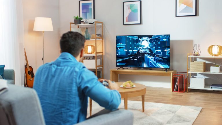 Audio-Anschlüsse am TV Ein Mann sitzt mit einem Controller auf dem Sofa und spielt ein Spiel auf dem Fernseher.