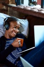 Eine Person liegt auf einem Sofa, hält eine Tasse in der Hand und videotelefoniert über ein Notebook.