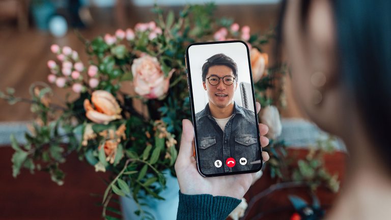 FaceTime Eine Person schaut in ihr Smartphone. Dort ist eine andere Person zu sehen. Sie kommunizieren per Videotelefonie.