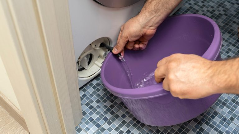 Flusensieb klemmt Eine Person lässt über den Ablass-Schlauch einer Waschmaschine überschüssiges Wasser in einen Eimer ab.