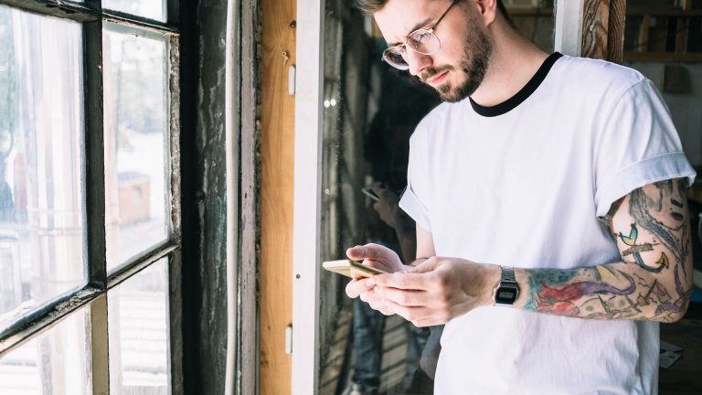 Eine Person steht vor einem Fenster und schaut auf ihr Android-Smartphone.