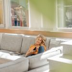 Eine Person sitzt auf einem Sofa. Von draußen scheint die Sonne in den Raum.