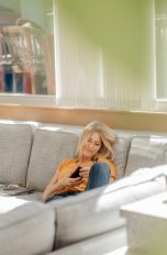 Eine Person sitzt auf einem Sofa. Von draußen scheint die Sonne in den Raum.