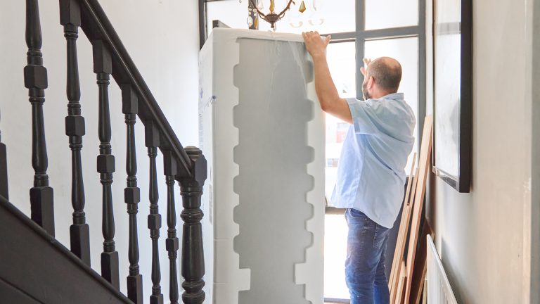 Kühlschrank anschließen Eine Person bringt einen neuen Kühlschrank in aufrechter Position ins Haus.