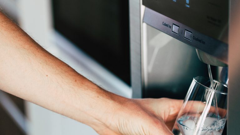 Kühlschrank anschließen Eine Person hält ein Glas unter einen Wasserstrahl, der aus einem Side-by-Side-Kühlschrank kommt.