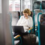Eine Person sitzt in der Bahn und hat einen Laptop auf dem Schoß.