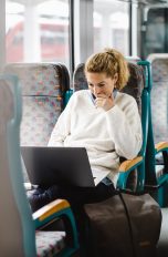 Eine Person sitzt in der Bahn und hat einen Laptop auf dem Schoß.