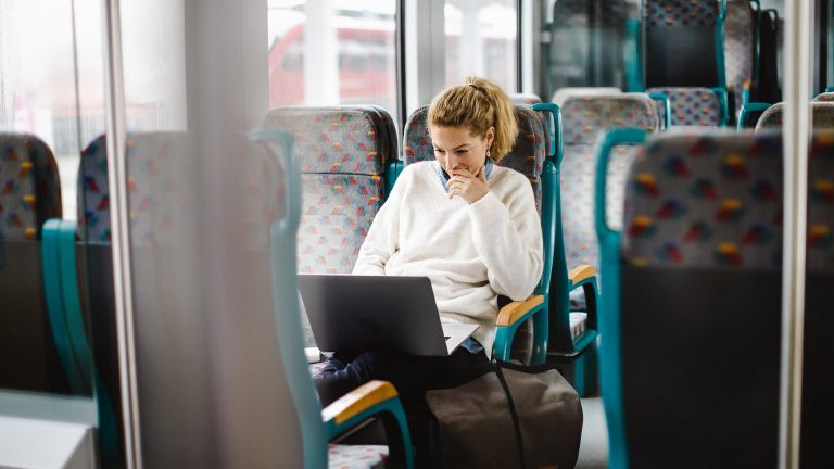 Eine Person sitzt in der Bahn und hat einen Laptop auf dem Schoß.