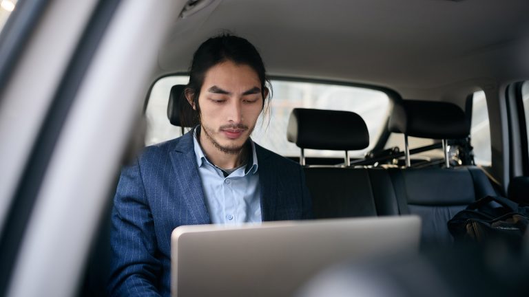 Sicher unterwegs Eine Person arbeitet mit einem Laptop auf dem Rücksitz in einem Auto.