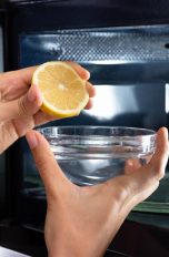 Eine Person träufelt den Saft einer Zitrone in eine Schüssel mit Wasser, ehe sie diese in die Mikrowelle gibt.