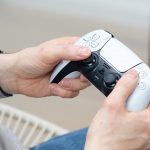 Eine Person hält einen DualSense-Controller der PS5 in Weiß in der Hand.