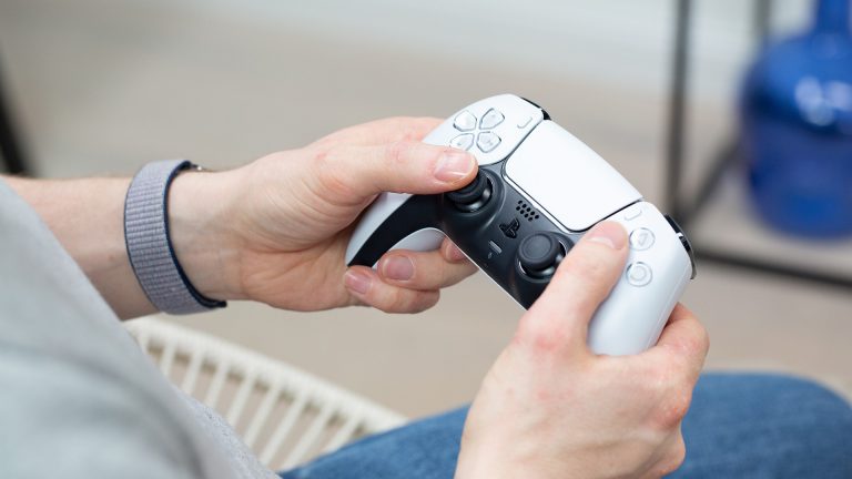 Eine Person hält einen DualSense-Controller der PS5 in Weiß in der Hand.