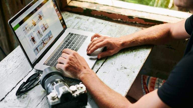 Eine Person bearbeitet an einem MacBook Bilder nach. Daneben liegt eine Kamera.