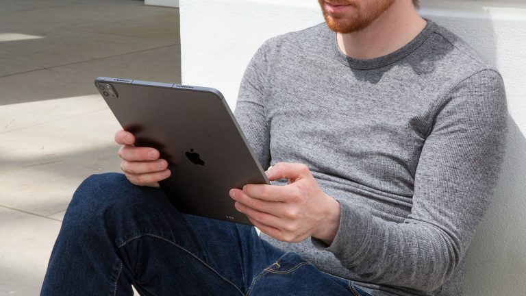 iPad Pro Sim Pin ändern Ein junger Mann lehnt an einer Hauswand, in den Händen hält er ein iPad.