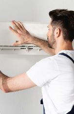 Eine Person auf einer Leiter schraubt die Abdeckung einer Split-Klimaanlage auf.