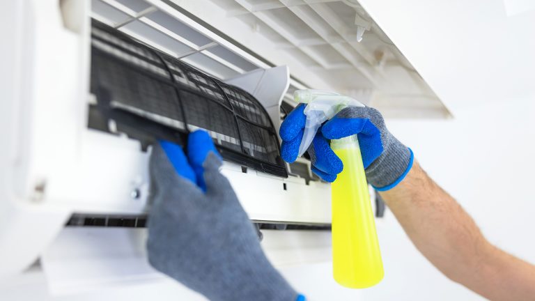 Klimaanlage reinigen Eine Person sprüht mit einem Spray eine Split-Klimaanlage von innen ein.