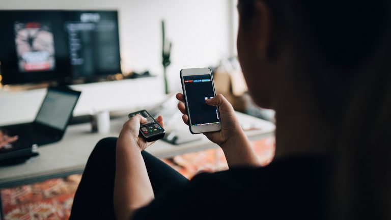 Smartphone als PC Eine Person sitzt vor einem Smart-TV und hat ein Smartphone in der Hand.