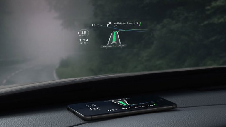 Smartphone Upcycling Ein Smartphone liegt auf dem Armaturenbrett eines Autos, direkt unter der Windschutzscheibe. Das Display projiziert den Fahrtverlauf einer Navigationsapp an die Scheibe.