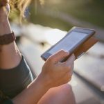 Eine Person sitzt im Freien und hält einen E-Book-Reader in der Hand.
