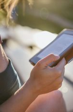 Eine Person sitzt im Freien und hält einen E-Book-Reader in der Hand.