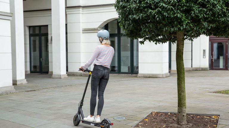 Mi Scooter 1S Eine Person fährt auf einem E-Scooter unter einem Baum hindurch.