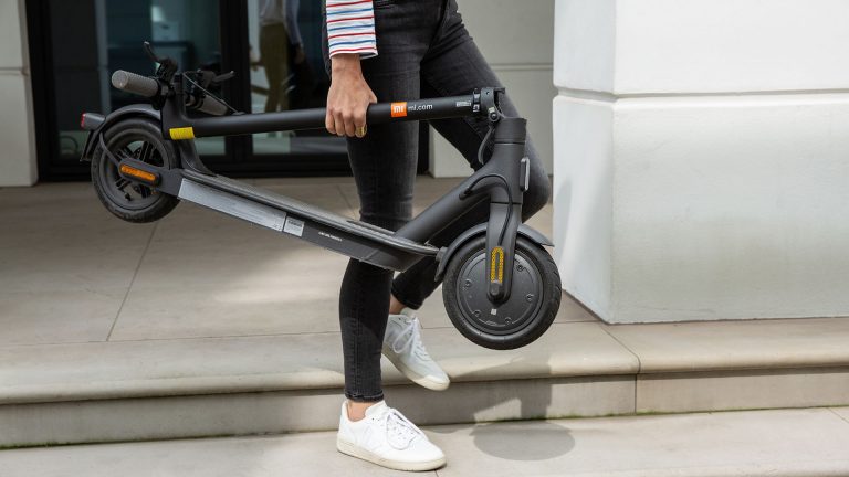 Mi Scooter 1S Eine Person läuft einige Stufen hinab. Dabei trägt sie einen zusammengeklappten E-Scooter in der Hand.