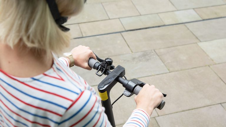 Mi Scooter 1S Eine Person steht auf einem E-Scooter. Zu sehen ist das Display im Lenker und die Geschwindigkeitsanzeige.