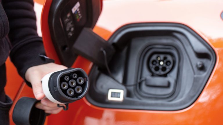 Elektroauto laden Eine Person hält einen Typ-2-Stecker in die Kamera. Im Hintergrund ist der dazugehörige Anschluss am Auto zu sehen.