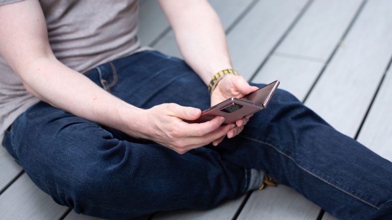 Samsung Galaxy Z Fold2 Eine Person sitzt auf dem Boden und hält ein halb geöffnetes Samsung Galaxy Z Fold2 in den Händen.