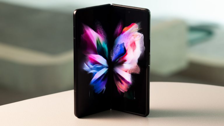 Samsung Galaxy Z Fold3 Das Samsung Galaxy Z Fold3 5G steht halb aufgeklappt hochkant auf einem Tisch.