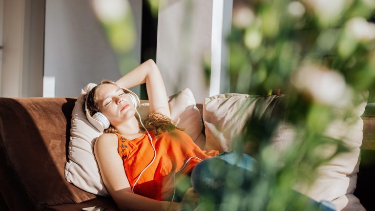 Spotify kündigen Eine Person liegt Kopfhörer tragend auf einem Sofa. Neben ihr liegt ein Smartphone, in das die Kopfhörer eingesteckt sind.