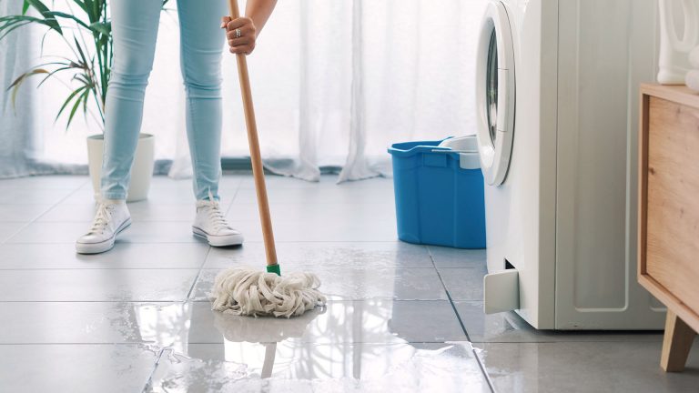 Waschmaschine pumpt nicht от Eine Person wischt mit einem Mopp Wasser auf, das aus einer Waschmaschine gelaufen ist.
