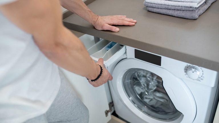 Waschmaschine stinkt Eine Person öffnet das Waschmittelfach an einer Waschmaschine und schaut hinein.