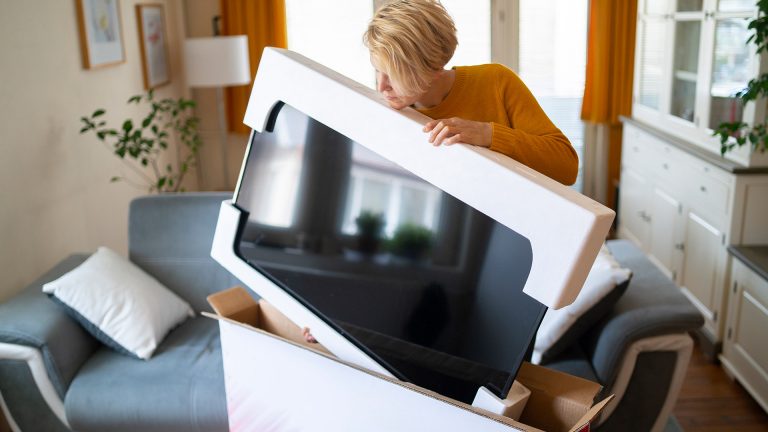 Fernseher oder Monitor an der Wand anbringen Eine Person entnimmt einen neuen Fernseher aus der Originalverpackung.
