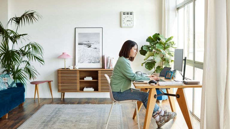 Fernseher oder Monitor an der Wand anbringen Eine Person sitzt an einem Schreibtisch. Ein Computer-Monitor ist mithilfe einer Tischhalterung daran befestigt.