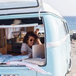 Eine Person in einem Kleinbus campt am Meer und surft mit einem Notebook im Internet.