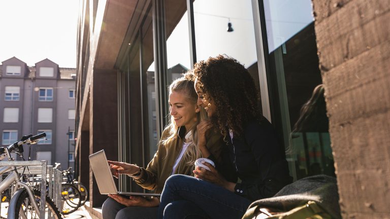 Internet-Stick Zwei Personen sitzen an einem Gebäude und schauen zusammen in einen Laptop.