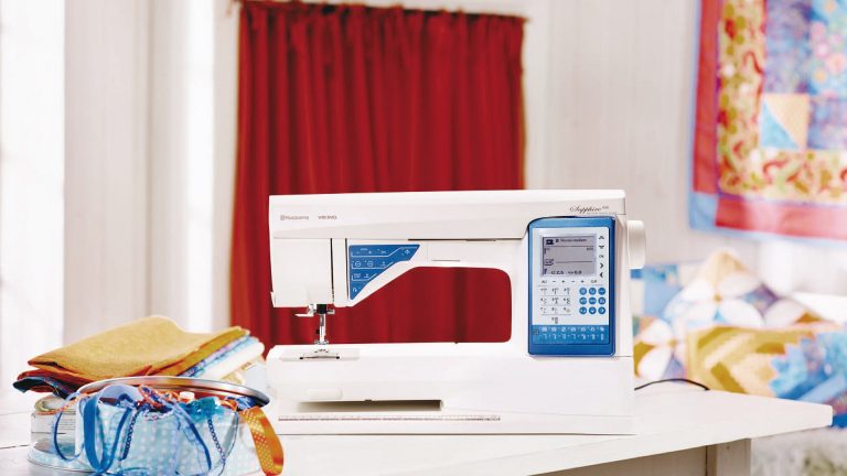 Husqvarna Viking Sapphire 930 Die Husqvarna Viking Sapphire 930 steht auf einem Tisch, daneben liegen mehrere Stoffe.