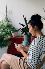Eine Person sitzt auf einem Balkon und hält ein Smartphone in der Hand.