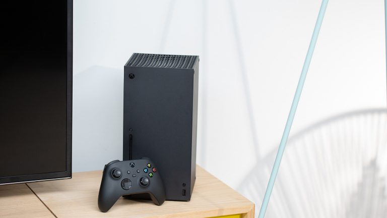 Sprachassistenten Eine Xbox Box Series X steht auf einem Holztisch neben einem Fernseher.